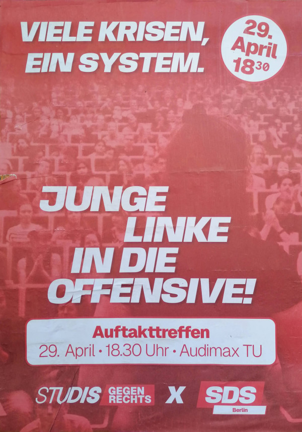 Ein rotes Poster mit weißem Text. Oben steht: "Viele Krisen, ein System." Rechts daneben ein weißer Kreis mit "29. April 18:30". Darunter der große Text: "Junge Linke in die Offensive!" Unten in einem weißen Kasten: "Auftakttreffen 29. April · 18.30 Uhr · Audimax TU". Ganz unten: "Studis gegen Rechts x SDS Berlin". Der Hintergrund zeigt viele Personen im Hörsaal.