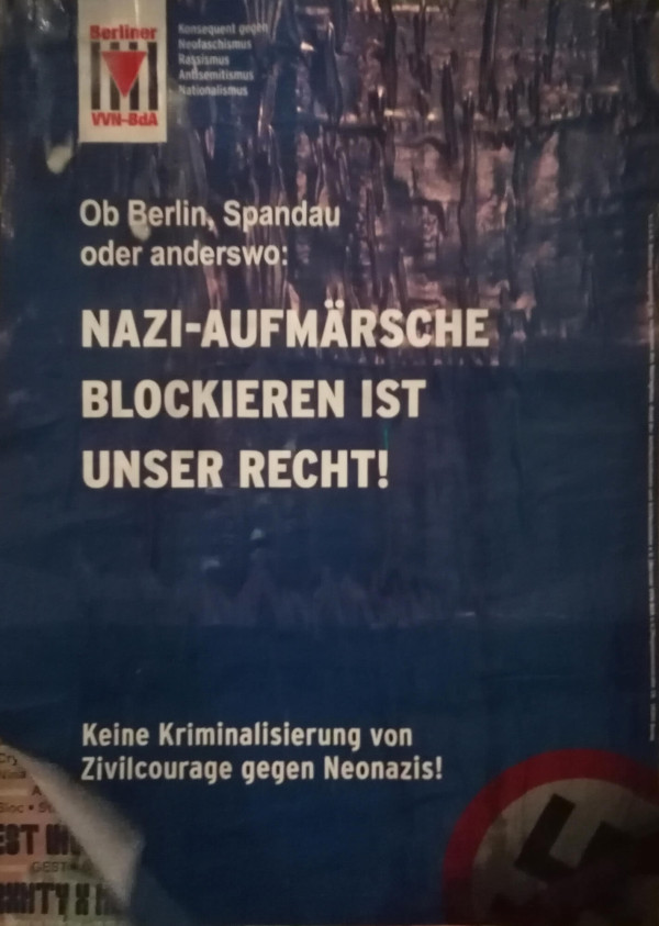 Ein blauer Poster mit weißem Text. Oben links befindet sich das Logo der "Berliner VVN-BdA" mit dem Text: "Konsequent gegen Neofaschismus, Rassismus, Antisemitismus, Nationalismus". Haupttext: "Ob Berlin, Spandau oder anderswo: Nazi-Aufmärsche blockieren ist unser Recht!" Unten steht: "Keine Kriminalisierung von Zivilcourage gegen Neonazis!" Unten rechts ist ein durchgestrichenes Hakenkreuz-Symbol.