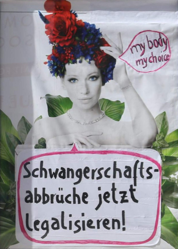 Eine schwarz-weiße Fotografie einer Frau mit einem farbenfrohen Blumenkranz aus roten und blauen Blumen auf dem Kopf. Rechts neben ihrem Kopf steht in einer rosa Sprechblase der englische Text "my body my choice". Im unteren Teil des Posters befindet sich ein weißes Schild mit dem deutschen Text "Schwangerschaftsabbrüche jetzt legalisieren!", umrandet von einer rosa Linie. Im Hintergrund sind grüne Blätter zu sehen.