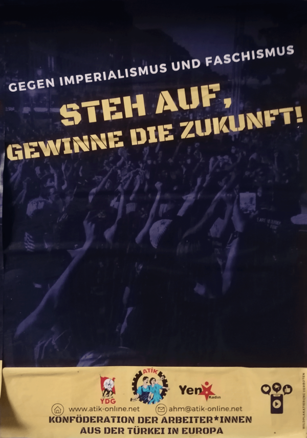 Ein Poster mit dunklem Hintergrund zeigt eine Menschenmenge mit erhobenen Fäusten. Oben steht in weißer Schrift "Gegen Imperialismus und Faschismus". In der Mitte befinden sich gelbe, blockartige Buchstaben mit dem Text "Steh auf, gewinne die Zukunft!". Unten ist ein gelber Streifen mit Logos und der Aufschrift "Konföderation der Arbeiter*innen aus der Türkei in Europa". Kontaktinformationen und Webseiten sind ebenfalls angegeben.